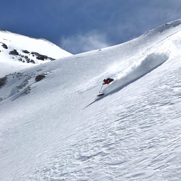 A skier enjoys bluebird powder near the OPUS Hut.